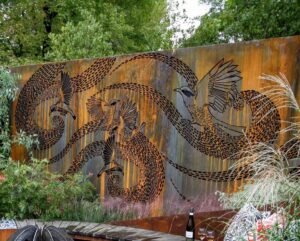 Corten steel wall with intricate wattlebird cut design surrounded by ornamental grasses in landscape garden