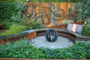 Curved timber seating around fire pit with large Corten steel wattlebird art screen backdrop in award-winning Nagasaki garden