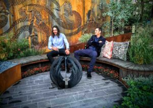 Two designers sitting on curved timber seating with wattlebird art screen backdrop in award-winning Nagasaki garden