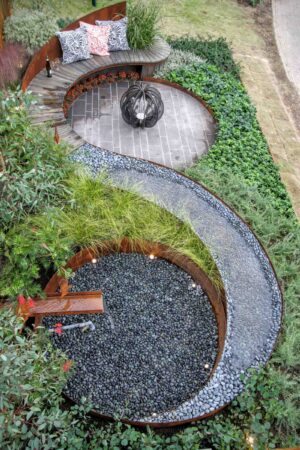 Aerial view of curved timber bench wrapping around stone paved area with sculptural fire feature in Nagasaki garden