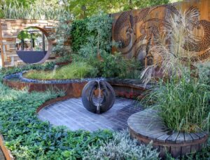 Black sculptural fire feature on stone paving with curved timber seating and native plantings in award-winning Nagasaki garden