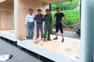 Four men posing together on wooden deck of modern pavilion structure in Nagasaki Japan during garden construction
