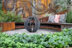 Laser-cut Corten steel wattlebird art screen behind curved timber seating with spherical water feature in Nagasaki garden