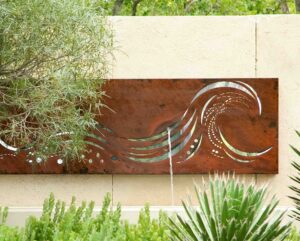 Corten steel wall panel with wave cut design mounted against rendered garden wall with planting