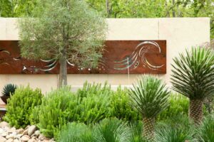 Corten steel wave sculpture integrated into cream masonry wall with native Australian plantings in Carlton, Victoria