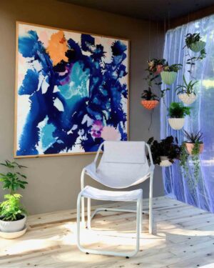 Large framed abstract painting in blues and orange above white chair with hanging plants in Melbourne-inspired balcony