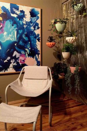 Interior corner featuring abstract blue artwork, modern white chair, and tiered hanging planters from We Heart Melbourne balcony garden
