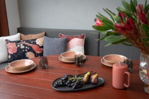 Custom blackbutt dining table and coral dinnerware on timber deck with curved seating and fresh flowers, Armstrong Street Ballarat