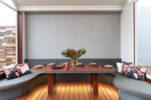 Built-in curved dining nook with grey upholstery, timber table, and floral arrangement in modern Ballarat home