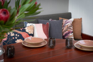 Custom curved blackbutt timber table built into corten steel seating with colorful cushions at Armstrong Street Ballarat