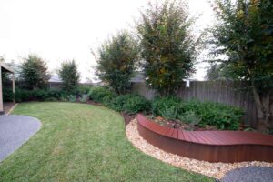 Curved corten steel seating with integrated fire pit in modern Ballarat backyard with lawn and mature trees