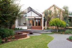 Modern Ballarat backyard with curved corten steel seating around central fire pit, timber deck and native landscaping