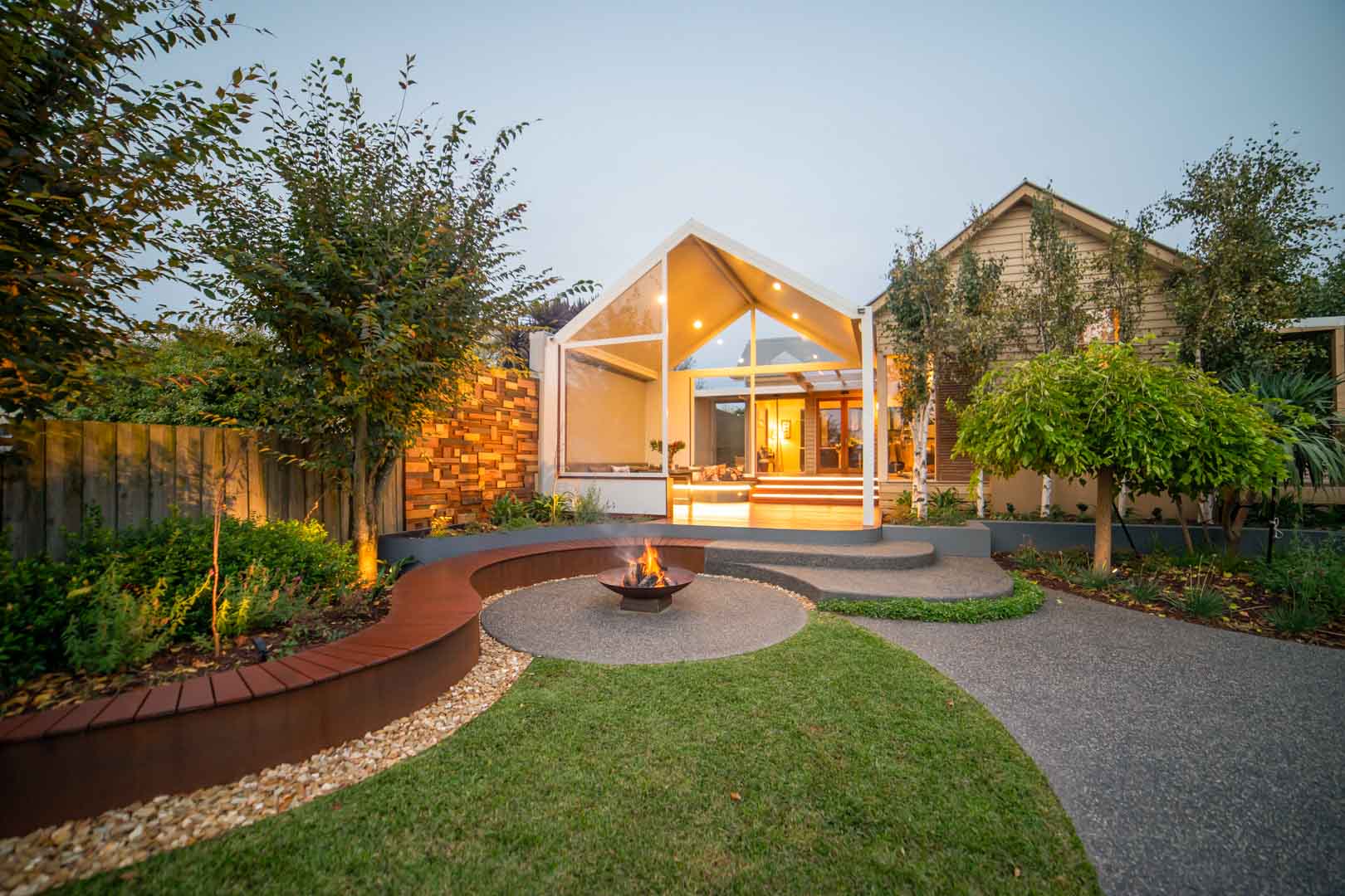 Curved corten steel seating around central fire pit with modern pavilion extension and landscaped garden in Ballarat