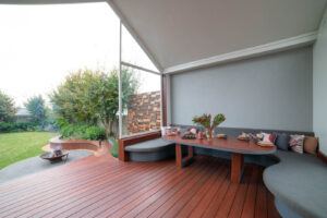 Covered outdoor dining area with curved built-in seating, blackbutt table, and fire pit overlooking landscaped garden in Ballarat