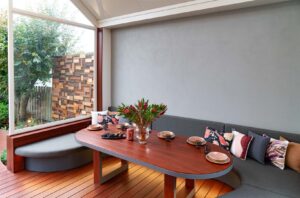 Built-in curved seating with blackbutt timber table around fire pit in covered outdoor dining area, Armstrong Street Ballarat