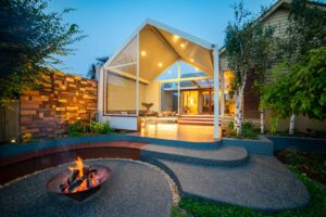 Modern outdoor pavilion with curved corten seating around fire pit and timber dining table at Armstrong Street Ballarat residence