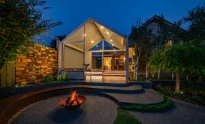 Modern pavilion with glass roof and curved corten seating around fire pit at twilight in Ballarat backyard