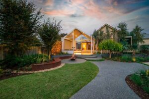 Curved corten steel seating around central fire pit with warm lighting at dusk in Ballarat backyard