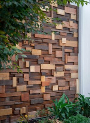 Mixed timber block feature wall with varied wood tones and textures surrounded by green foliage in Ballarat garden