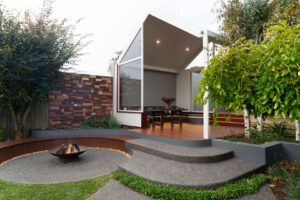 Modern outdoor dining pavilion with curved concrete seating, central fire pit and timber decking in Ballarat backyard