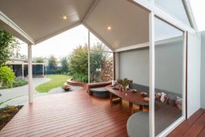Covered timber deck with curved fire pit seating and dining table overlooking landscaped backyard in Ballarat