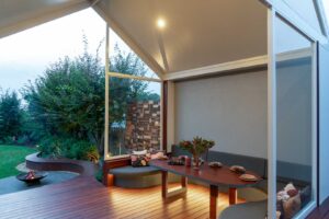 Covered outdoor dining area with curved seating, timber table and fire pit at Armstrong Street Ballarat residence