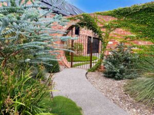 Gravel garden path with blue spruce, brick archway covered in climbing plants and colourful summer garden beds, Victoria