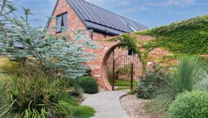 Curved brick archway entrance with steel gate leading through native plantings at Mount Buninyong country garden