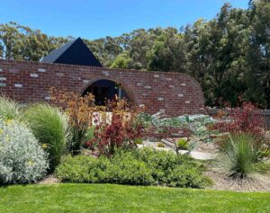 Curved brick wall with arched moon gate opening framed by native plantings and ornamental grasses in Buninyong garden