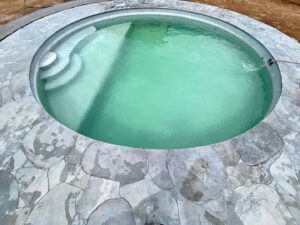 Circular swimming pool with natural stone coping and green water, surrounded by curved stone paving in Mount Buninyong