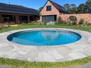 Large circular swimming pool with natural stone coping surrounded by native plantings at Mount Buninyong country property
