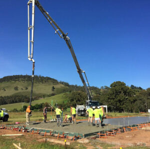 Construction crew pouring concrete for circular swimming pool foundation using concrete pump truck in Buninyong