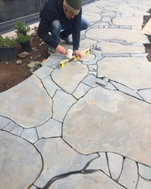 Worker installing irregular flagstone paving with spirit level at Mount Buninyong country estate garden project