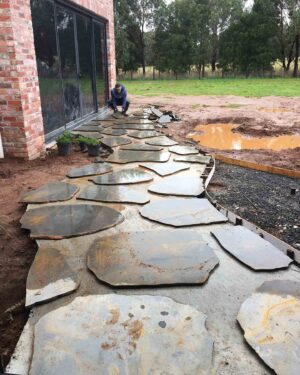 Large irregular flagstone pavers being laid on concrete base with worker positioning stones in Mount Buninyong