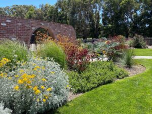 Curved native garden border with colourful plantings beside brick archway and lawn at Mount Buninyong country property