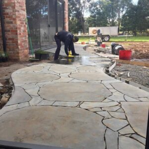 Worker installing irregular natural stone paving beside brick building in Mount Buninyong country garden construction