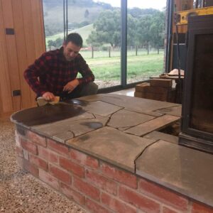 Man in flannel shirt laying sandstone slabs on brick pizza oven base in Mount Buninyong country garden construction