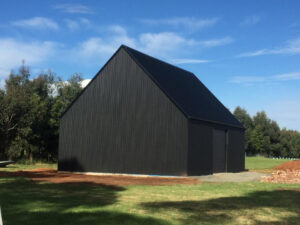 Large dark corrugated steel agricultural shed with gabled roof under construction on rural Mount Buninyong property