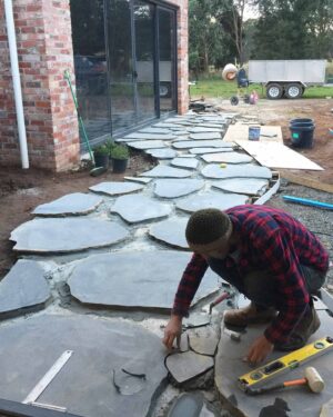 Worker installing natural stone paving pieces outside brick house with glass doors in Mount Buninyong