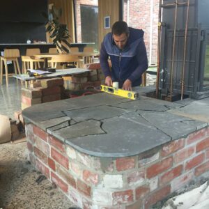 Craftsman using spirit level on slate-topped pizza oven with brick base during construction at Mount Buninyong property