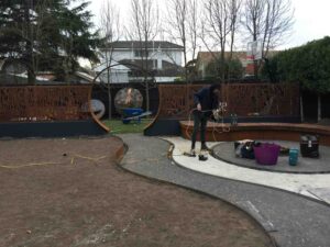 Workers installing curved corten steel edging and structures in residential garden under construction