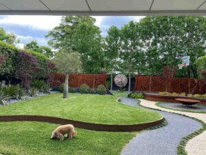 Curved grass lawn with corten steel edging, winding path, and decorative screening panels in modern backyard landscape