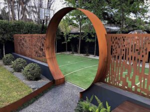 Circular corten steel moon gate frames entry to artificial turf sports court with perforated screening panels
