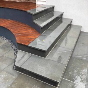 Concrete steps leading to timber decking with curved corten steel detail and white wall backdrop