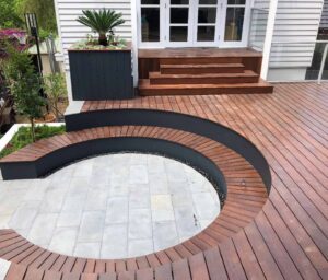 Curved merbau timber deck surrounding circular pool with white stone paving and black corten steel edging