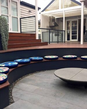 Sunken circular conversation pit with colorful tropical print cushions arranged around curved seating wall on timber deck