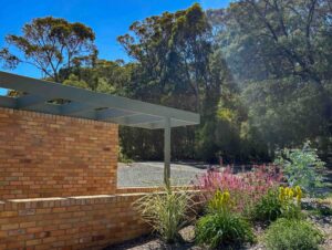 Red brick wall with white steel pergola frame and native plantings in foreground with eucalyptus trees behind