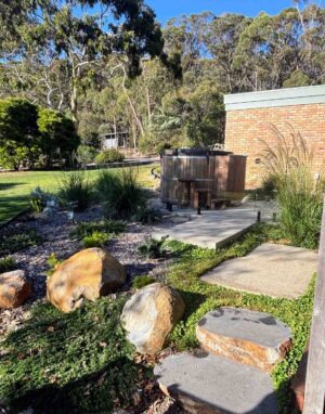 Large natural stone boulders embedded in landscaped garden with native grasses, concrete pathways, and brick wall background
