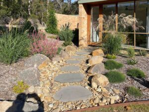 Large flat stone stepping stones set in gravel with ornamental grasses and native plants leading to modern house entrance